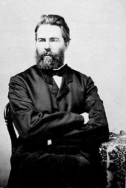 A young bearded man seated with arms crossed for a black-and-white portrait.