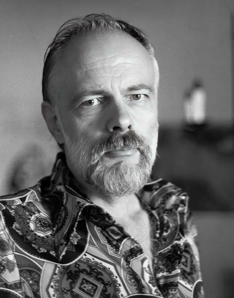 Black and white photograph of a white man with a full white beard, wearing a forlorn expression.